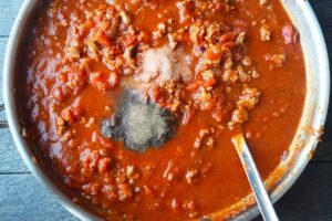 Salt and pepper added to spaghetti sauce in a skillet.