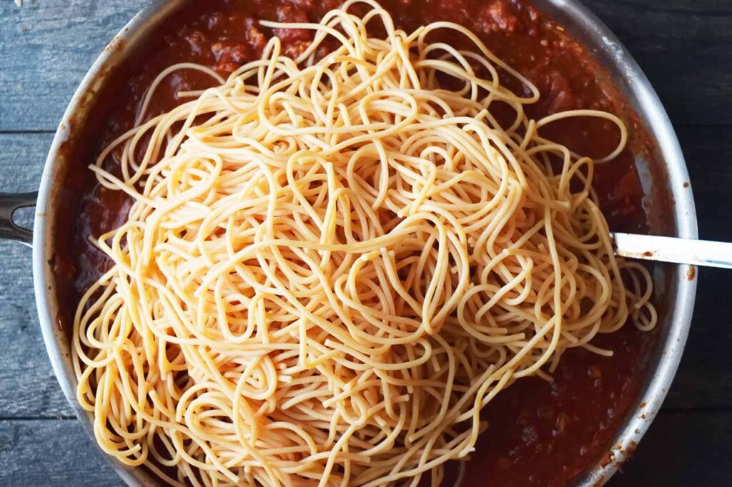 Pasta added to spaghetti sauce in a skillet.