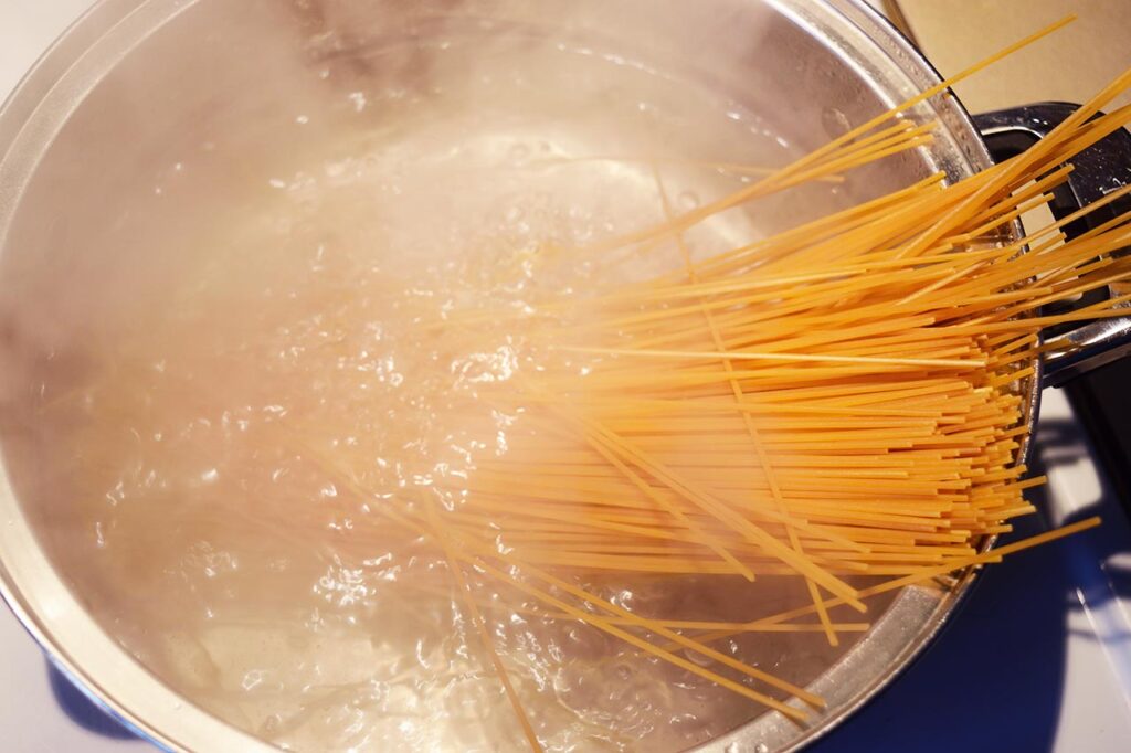 Raw spaghetti added to a pot of salted, boiling water.