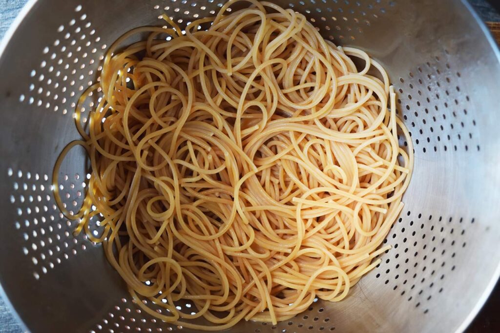 Cooked spaghetti pasta draining in a strainer.