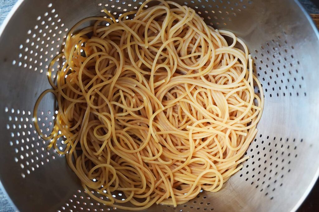 Cooked spaghetti pasta draining in a strainer.