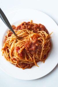 An overhead view of a white plate with a nest of of spaghetti and a fork standing up in the pasta.