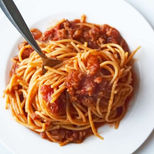 An overhead view of a white plate with a nest of of spaghetti and a fork standing up in the pasta.