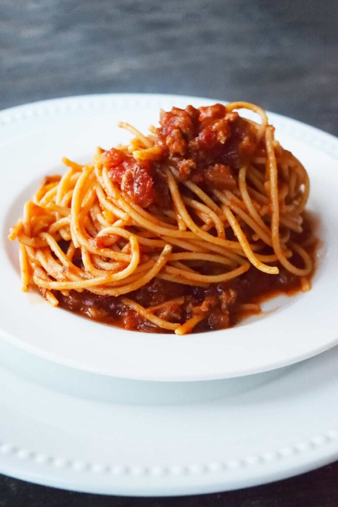 A white plate of spaghetti on a gray surface.