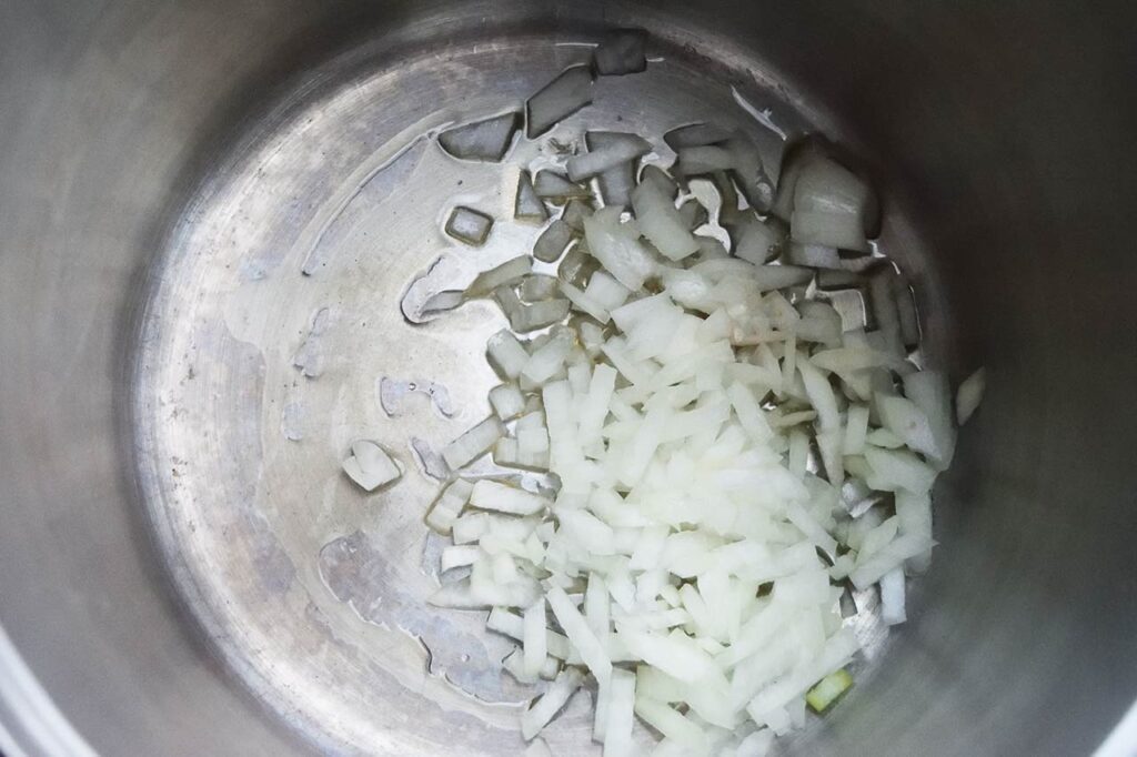 Chopped onions sitting in oil in a pot.