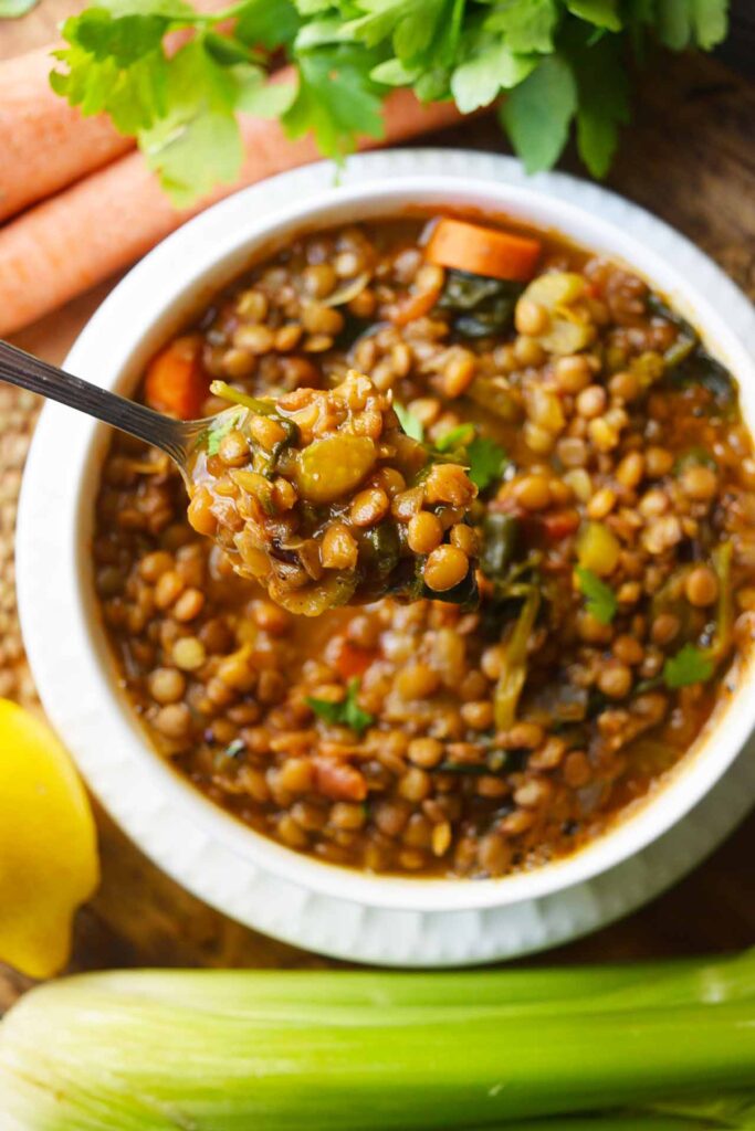 An overhead view of a spoon lifting a spoonful of Spinach Lentil Soup our of a white bowl.