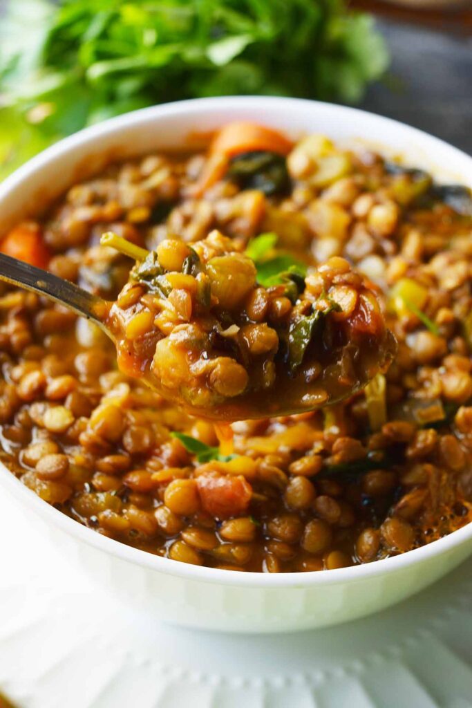 An side view of a spoon lifting a spoonful of Spinach Lentil Soup our of a white bowl.