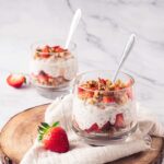 Two glasses on a marble countertop. On on the counter and one on a cutting board. Both are filled with Strawberry Chia Pudding.