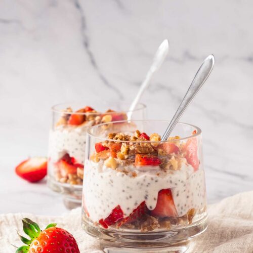 A front view of two glasses filled with Strawberry Chia Pudding. Spoons stand up in the glasses.