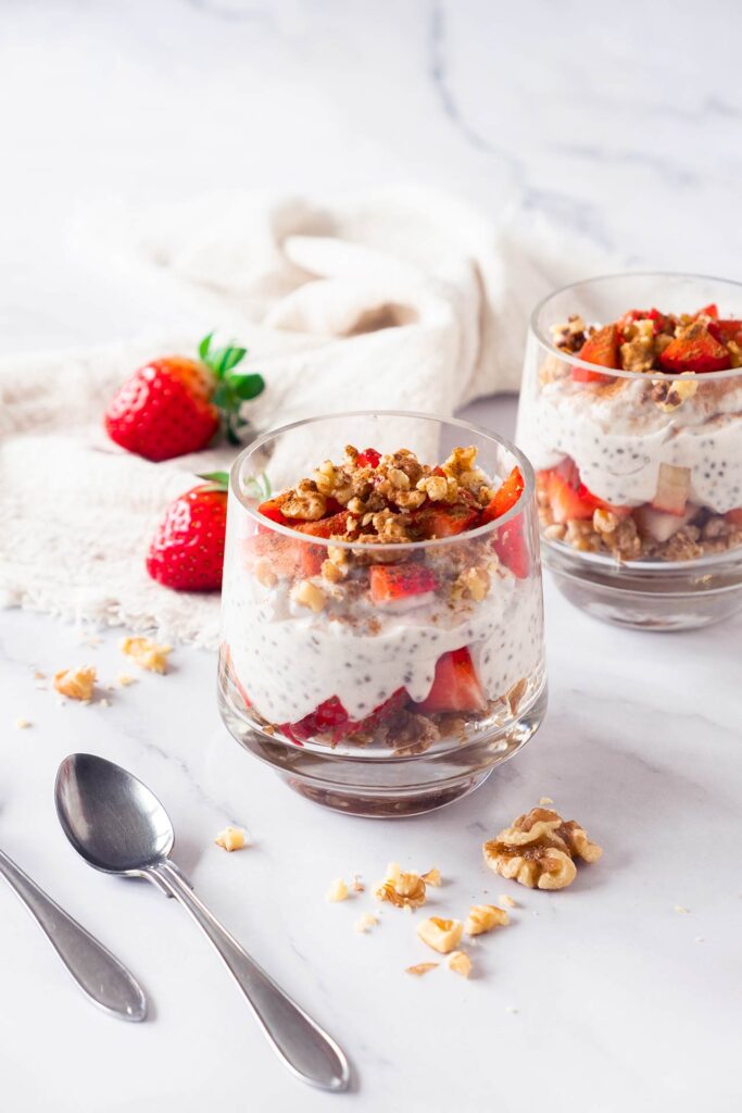 Two clear glasses filled with Strawberry Chia Pudding on a white marble surface.