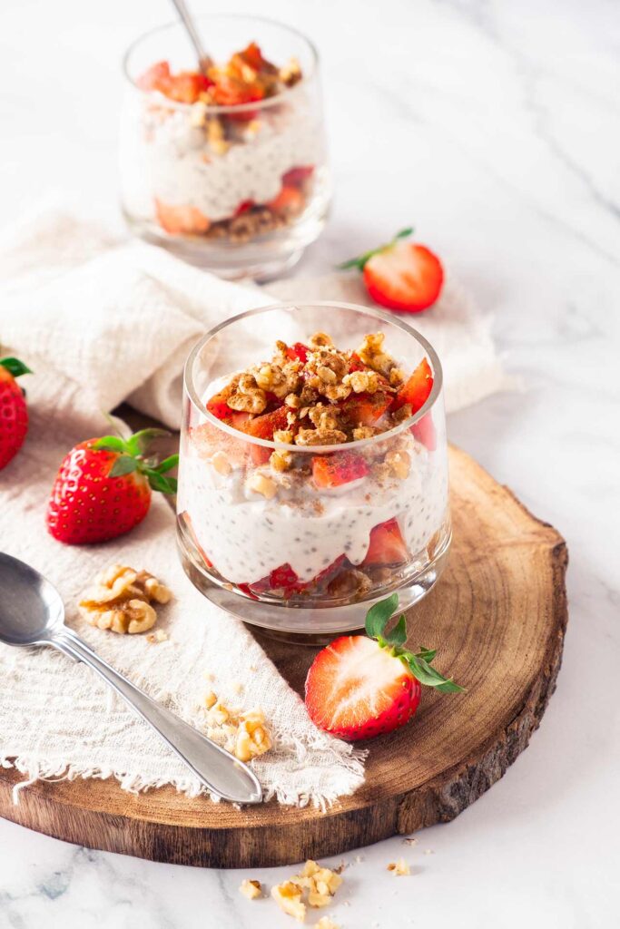 A partially overhead view of a glass filled with Strawberry Chia Pudding, sitting on a cutting board.