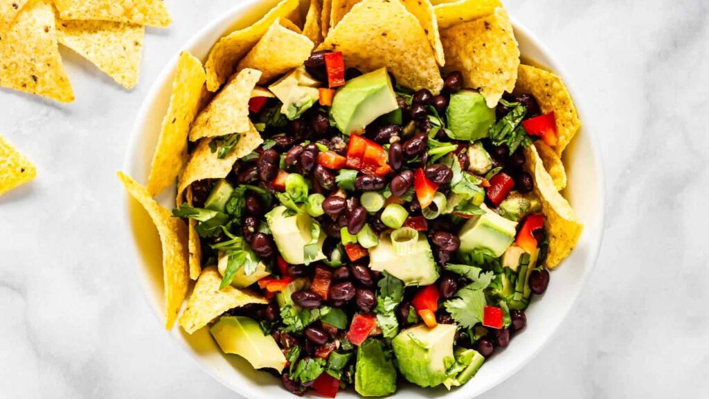 An overhead view of a white bowl filled with avocado black bean salsa and a few corn chips.