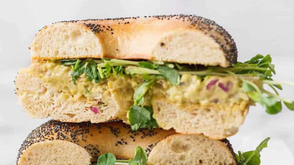 An Avocado Chickpea Salad Sandwich stacked up on a white background.