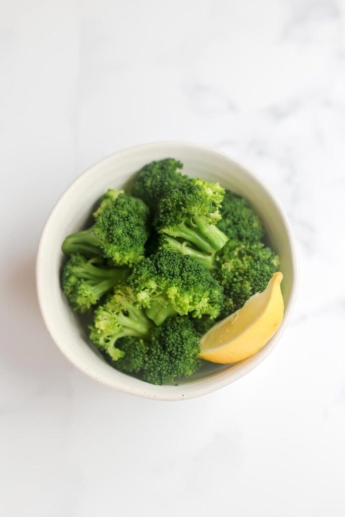 Boiled broccoli in a bowl with a lemon wedge.