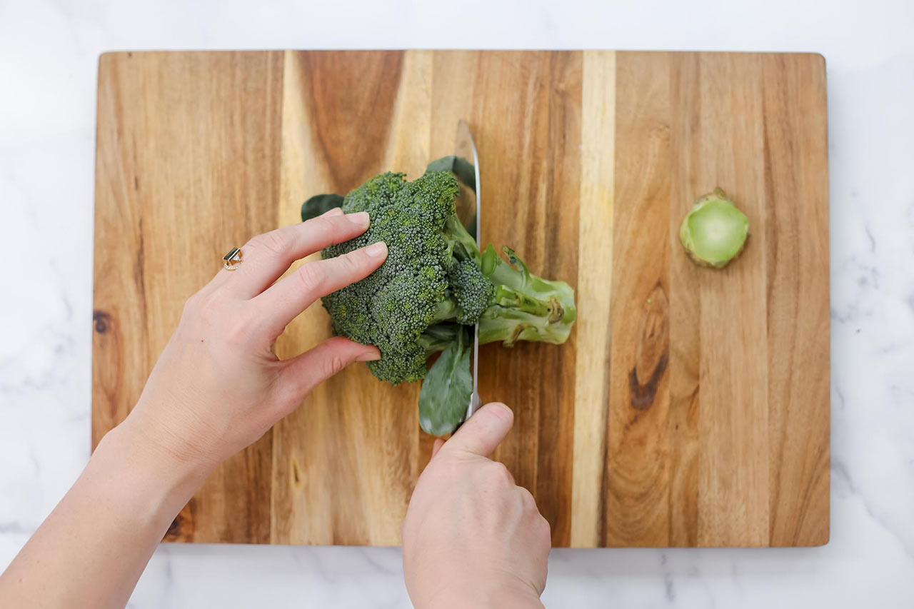 Cutting a broccoli floret on a wood cutting board.