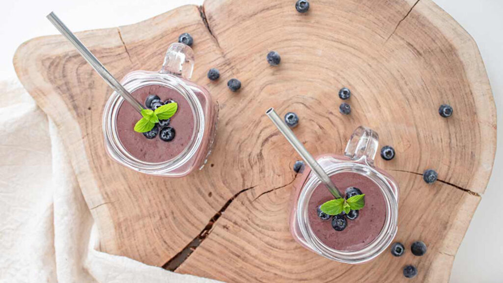 An overhead view of two glass mugs filled with Acai Smoothie, garnished with fresh blueberries and fresh mint leaves.