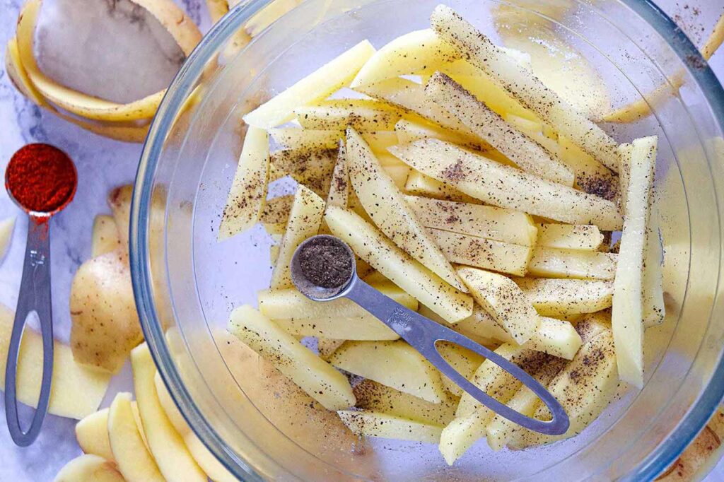 Sprinkling seasoning over fries in a mixing bowl.