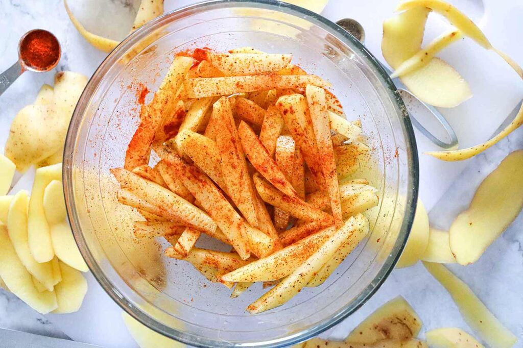 Seasoned and oiled fries in a mixing bowl.