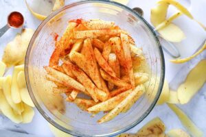 Seasoned and oiled fries in a mixing bowl.