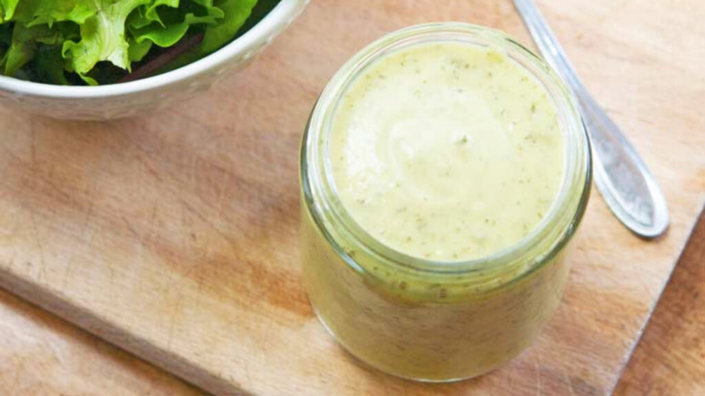 An open jar filled with Avocado Ranch Dressing on a cutting board.