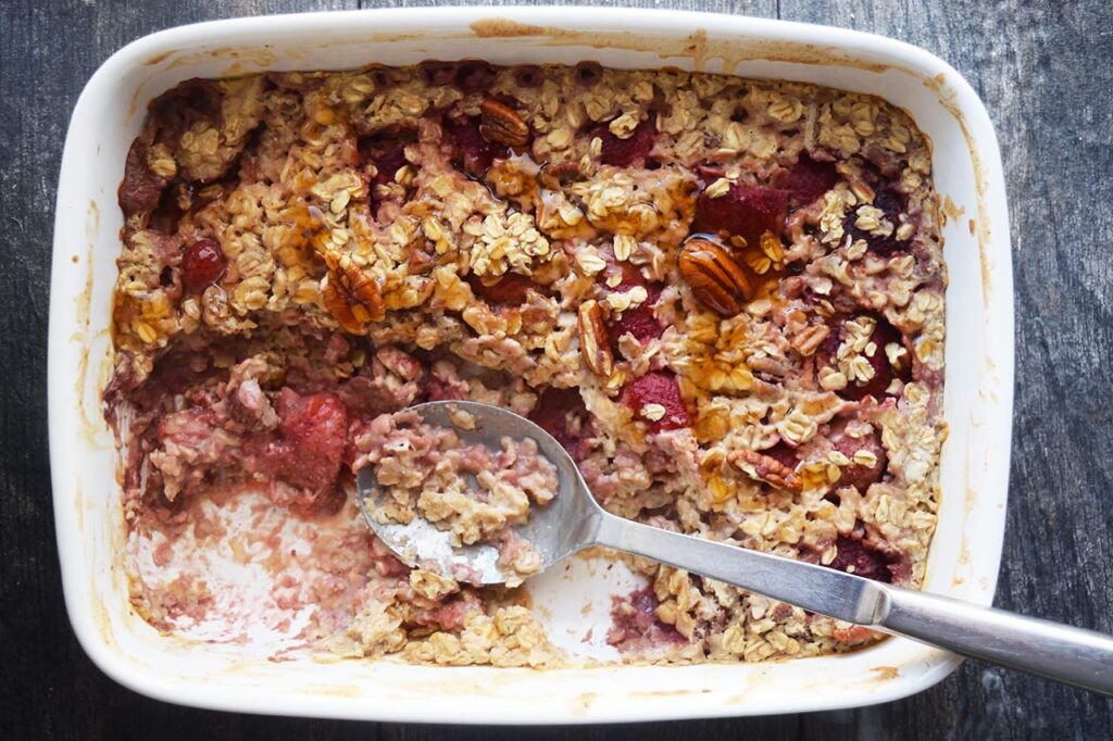 An overhead view of a white casserole dish with a portion of Baked Oatmeal With Strawberries removed.