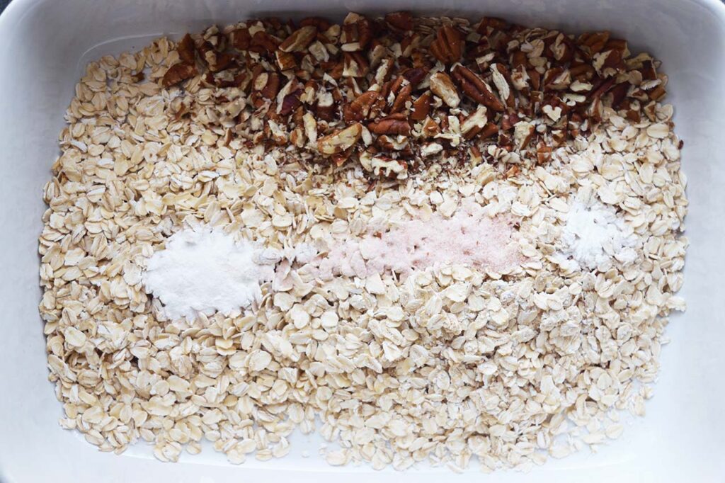 Oats, nuts, salt and baking powder in a white casserole dish, unmixed.