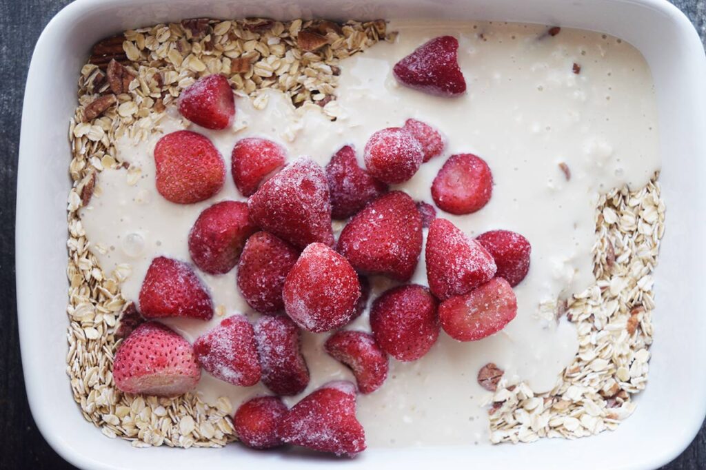 frozen strawberries added to a white casserole dish with both wet and dry ingredients unmixed.