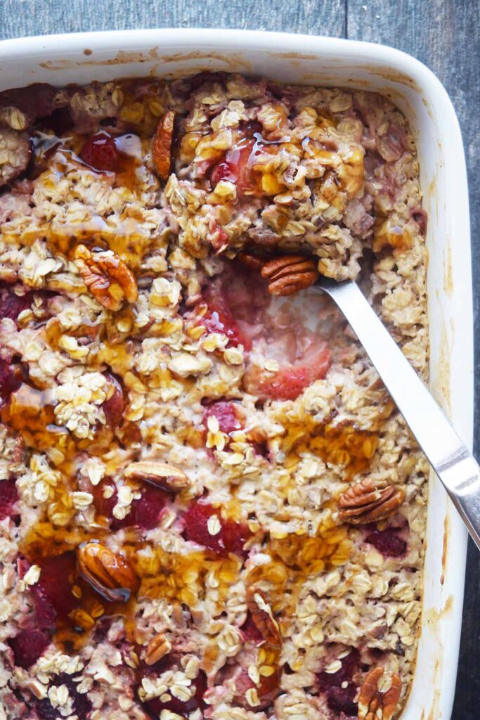 A serving spoon pushed into the Baked Oatmeal With Strawberries casserole.