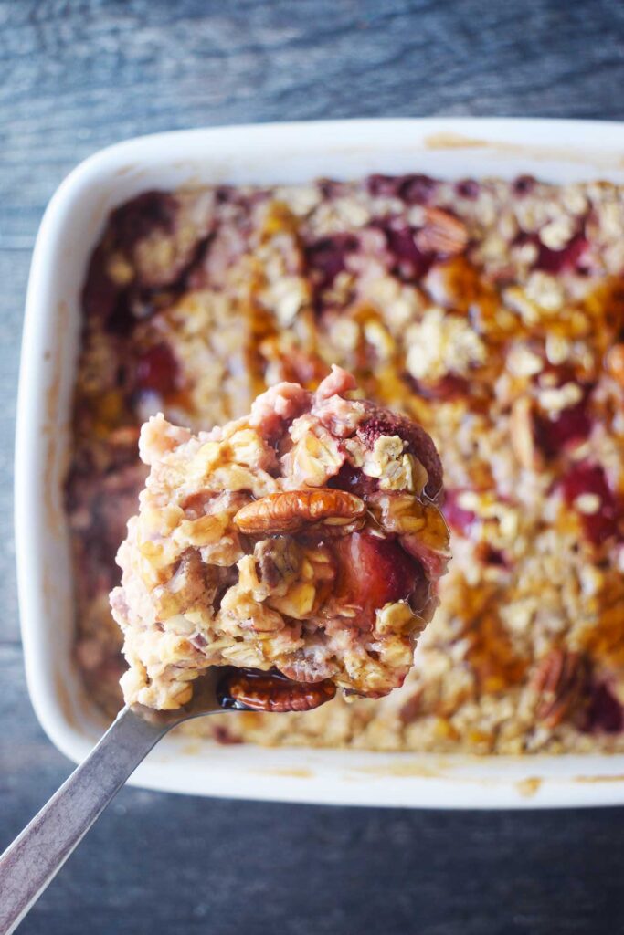 A spoon lifts some Baked Oatmeal With Strawberries out of a casserole dish full of it.