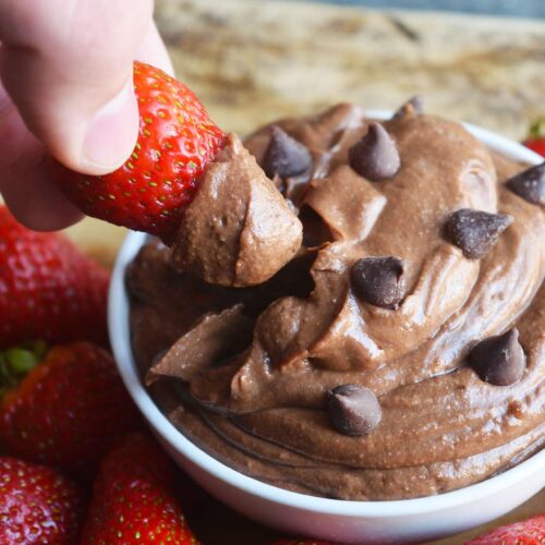 A hand dipping a strawberry into a bowl of brownie batter dip.