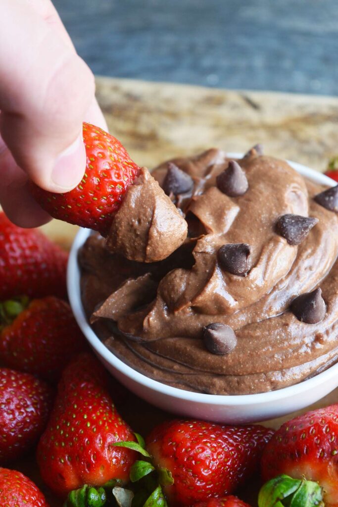 A hand dipping a strawberry into a bowl of brownie batter dip.