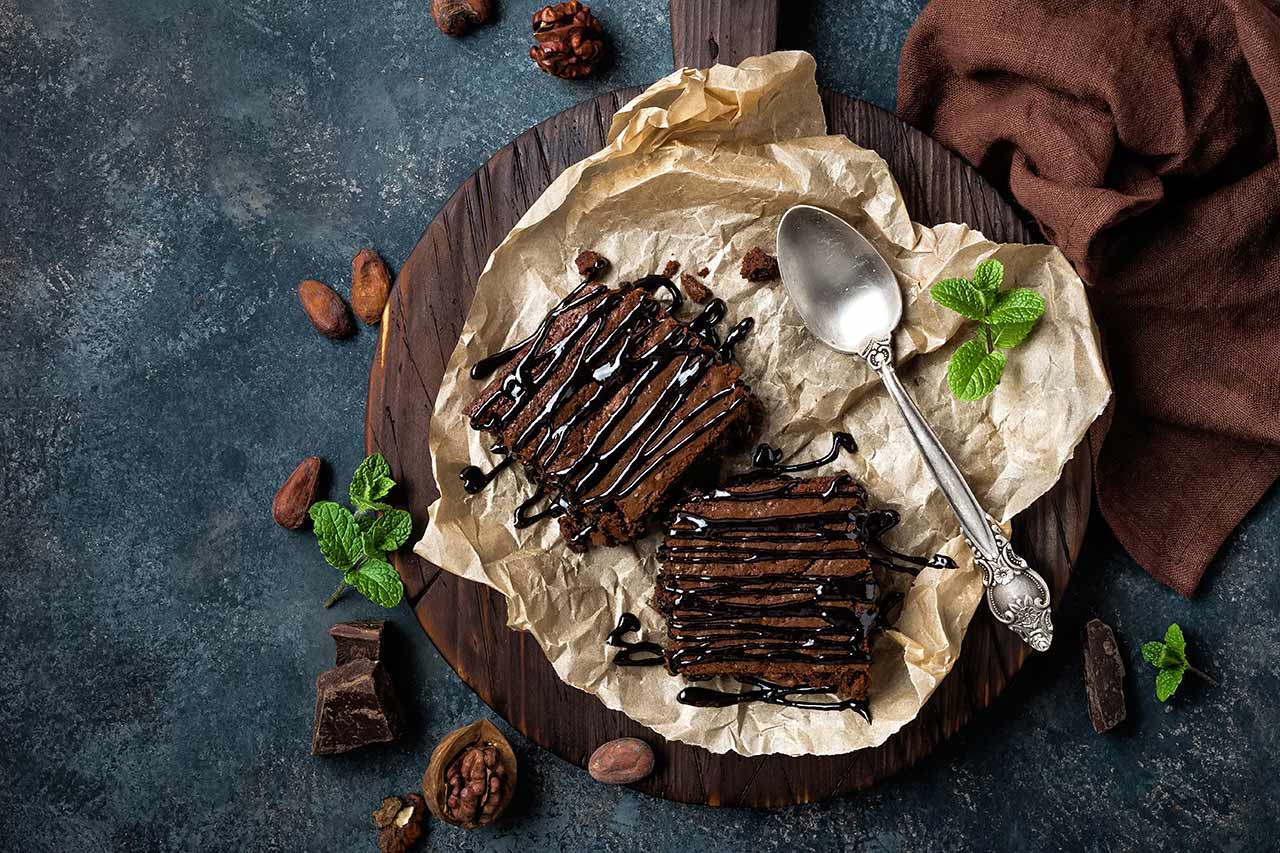 An overhead view of two brownies on a piece of parchment paper with chocolate sauce drizzled over the tops.