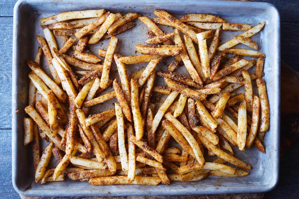 A baking sheet filled with seasoned, frozen fries.