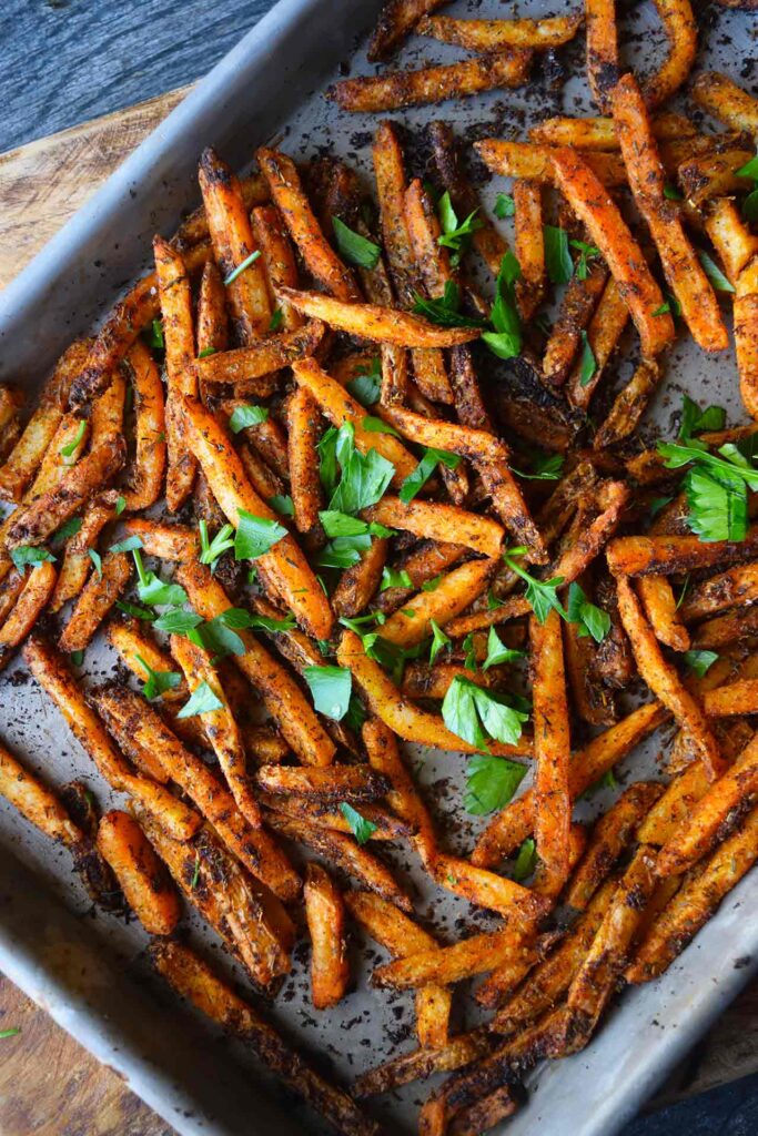 An overhead view of a baking sheet filled with Cajun Fries and topped with fresh, chopped parsley.