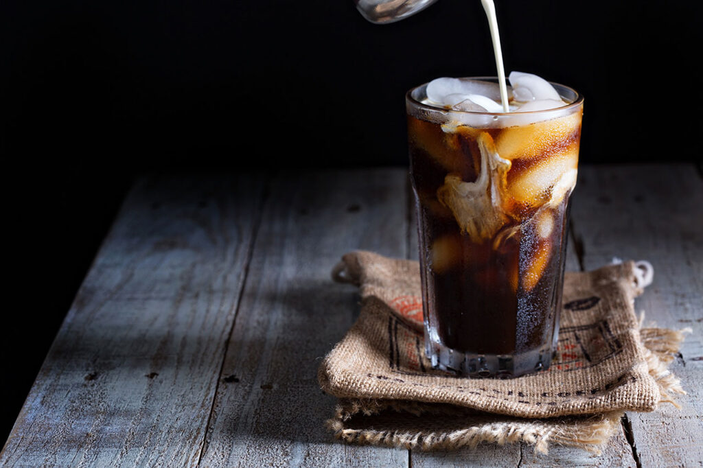 Cold foam being poured into iced coffee.