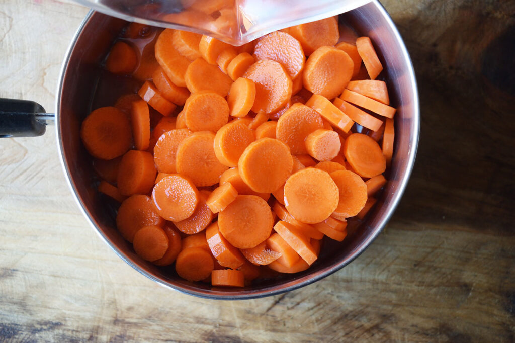 Broth added to sliced carrots in a pot.