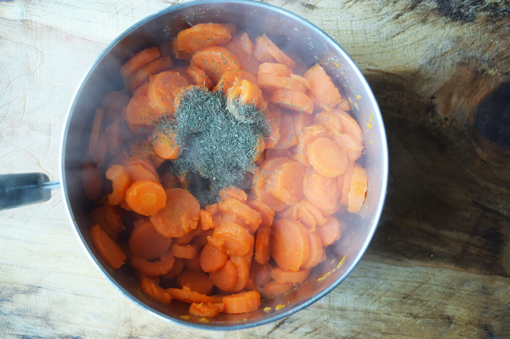 Dill added to cooked carrots in a pot.
