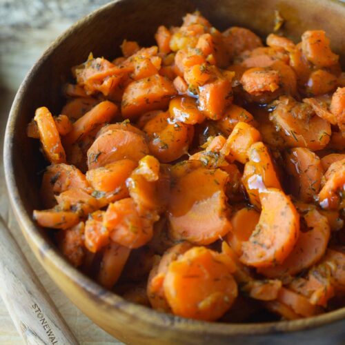 A wooden bowl filled with dill carrots sitting on a wood cutting board.