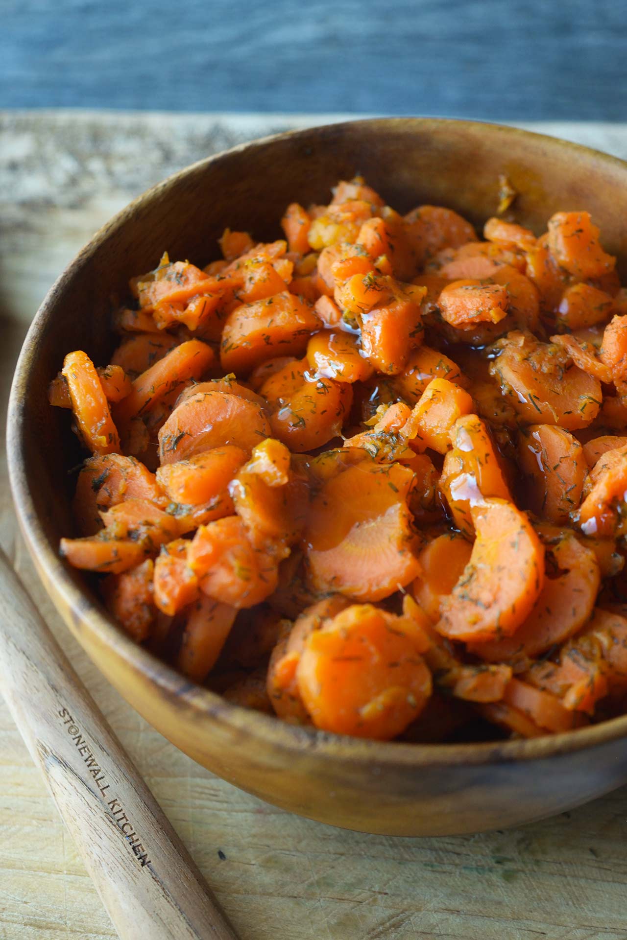 A wooden bowl filled with dill carrots sitting on a wood cutting board.