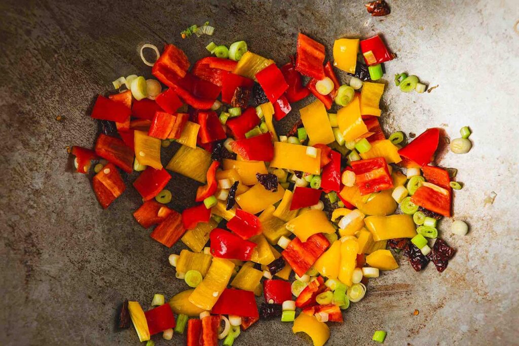 Peppers and green onions slices added to chopped chillies in a wok.