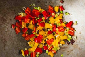 Peppers and green onions slices added to chopped chillies in a wok.