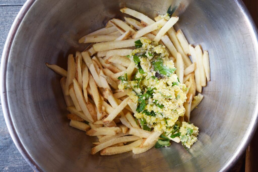 Garlic Fries seasoning mix added to cut fries in a mixing bowl.