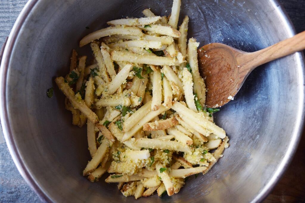 Garlic Fries coated in seasoning in a mixing bowl.