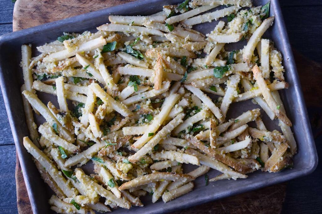 Seasoned Garlic Fries spread out over a sheet pan for baking.