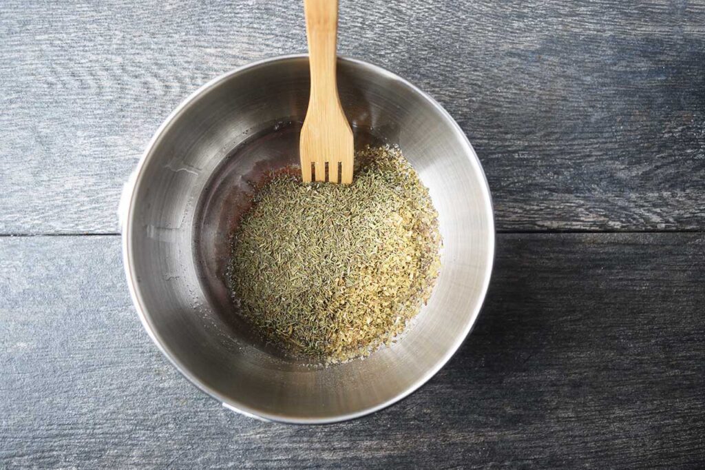 Spices and oil in a metal mixing bowl, unmixed.