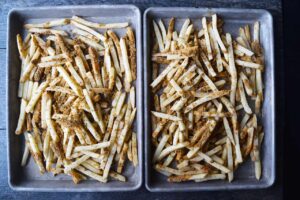 Seasoned fries spread out over two sheet pans.