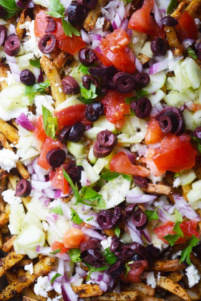 A closeup of Greek fries topped with fresh vegetable toppings.