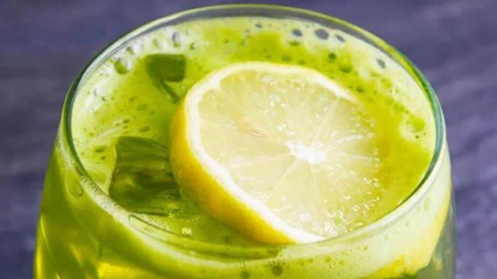 A closeup of a glass of green lemonade garnished with a lemon slice.