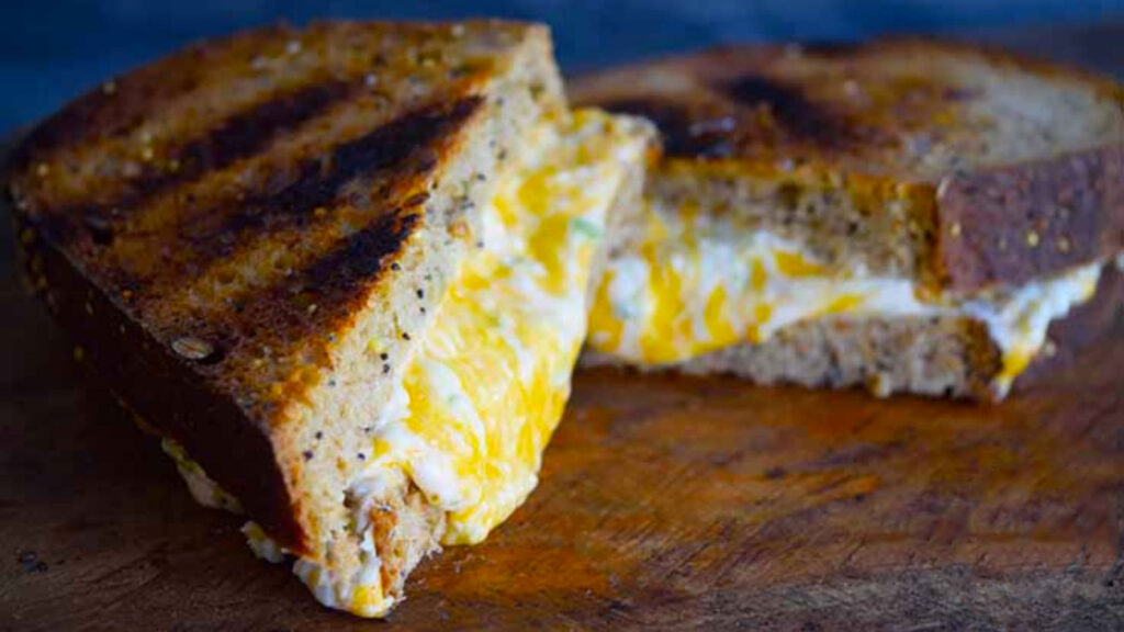 A cut Jalapeno Popper Grilled Cheese Sandwich lays on a cutting board with melted cheese oozing out of it.