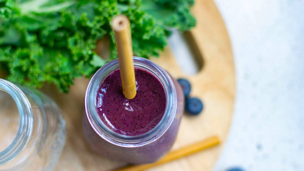 An overhead view of a glass bottled filled with Kale Blueberry Smoothie with a straw sitting in it.